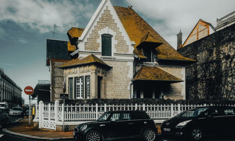 A house with a white picket fence and cars parked in front of it