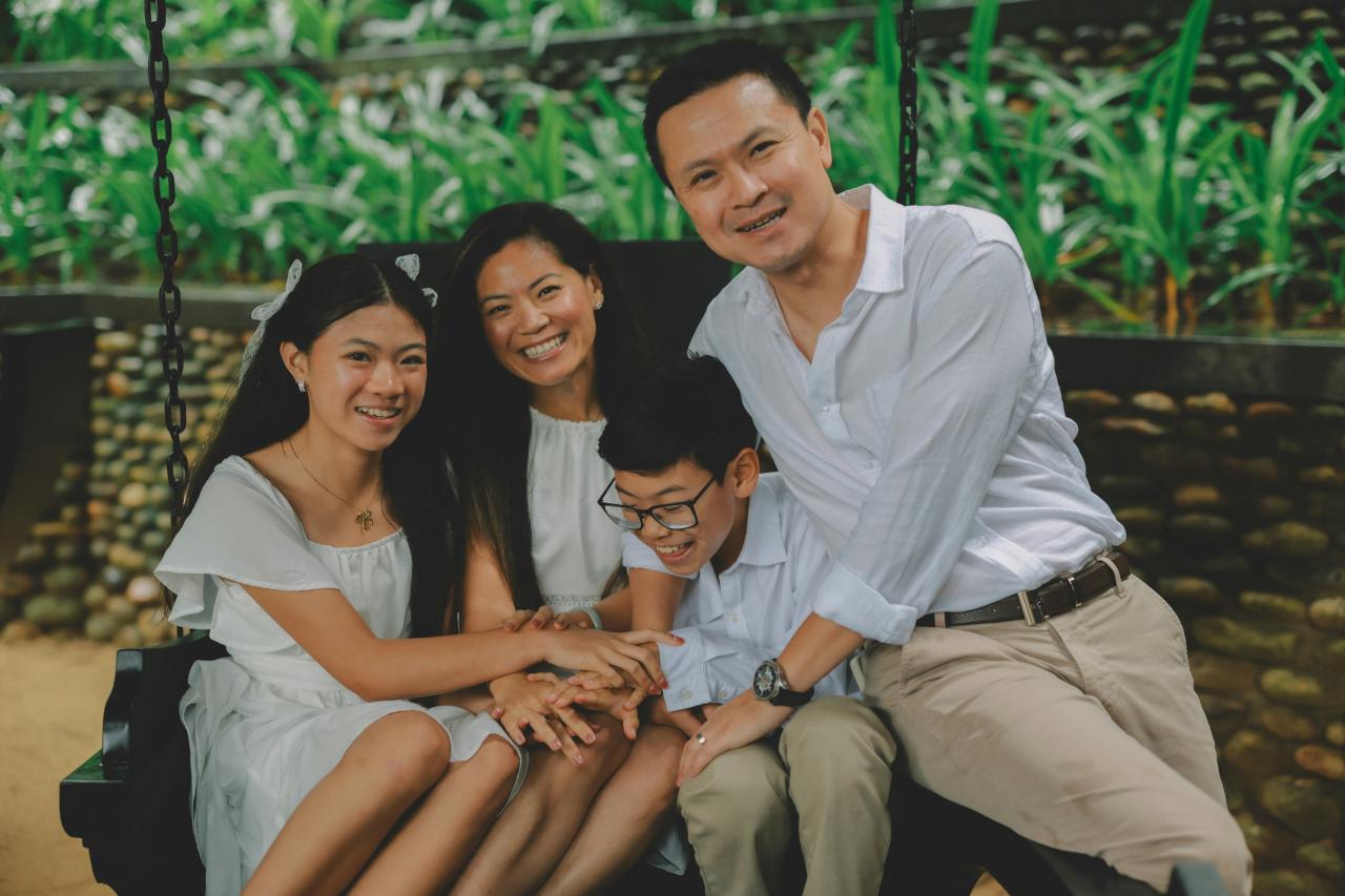 A happy family of four sitting on a swing outdoors.